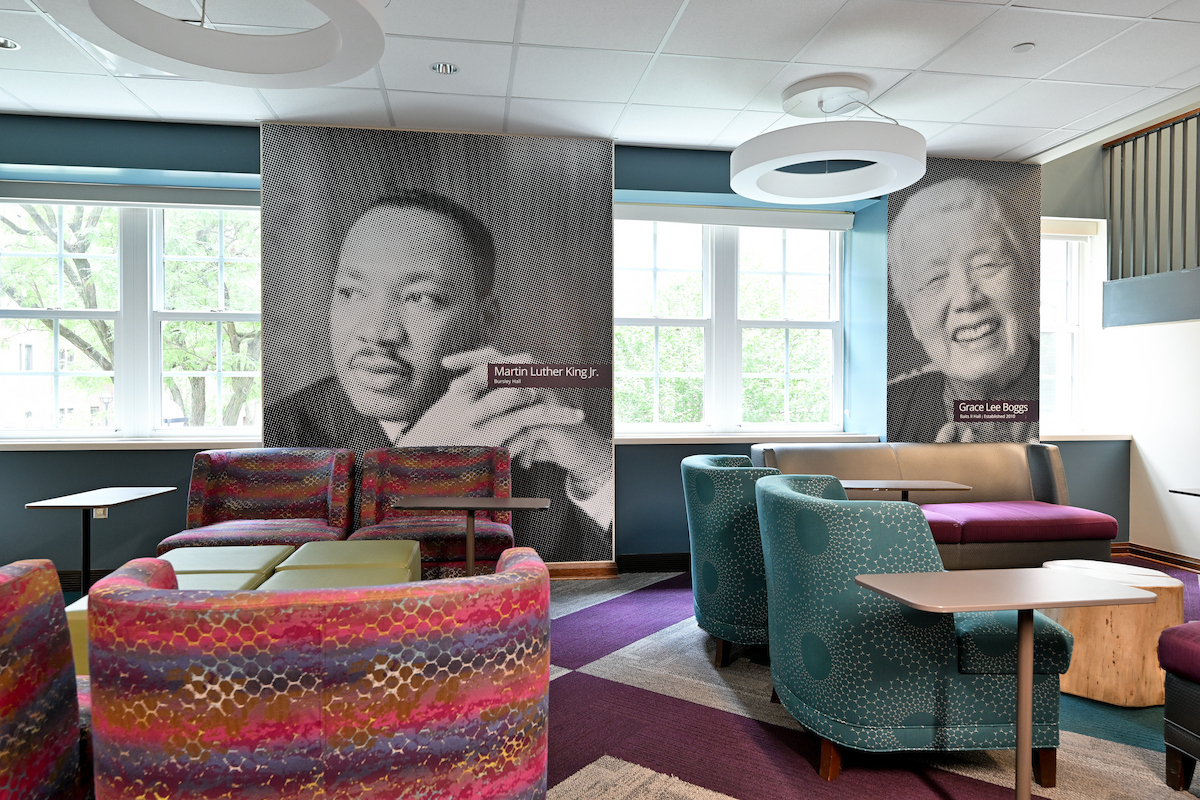 A modern lounge features colorful upholstered seating and large black-and-white portraits of Martin Luther King Jr. and Grace Lee Boggs on the walls.